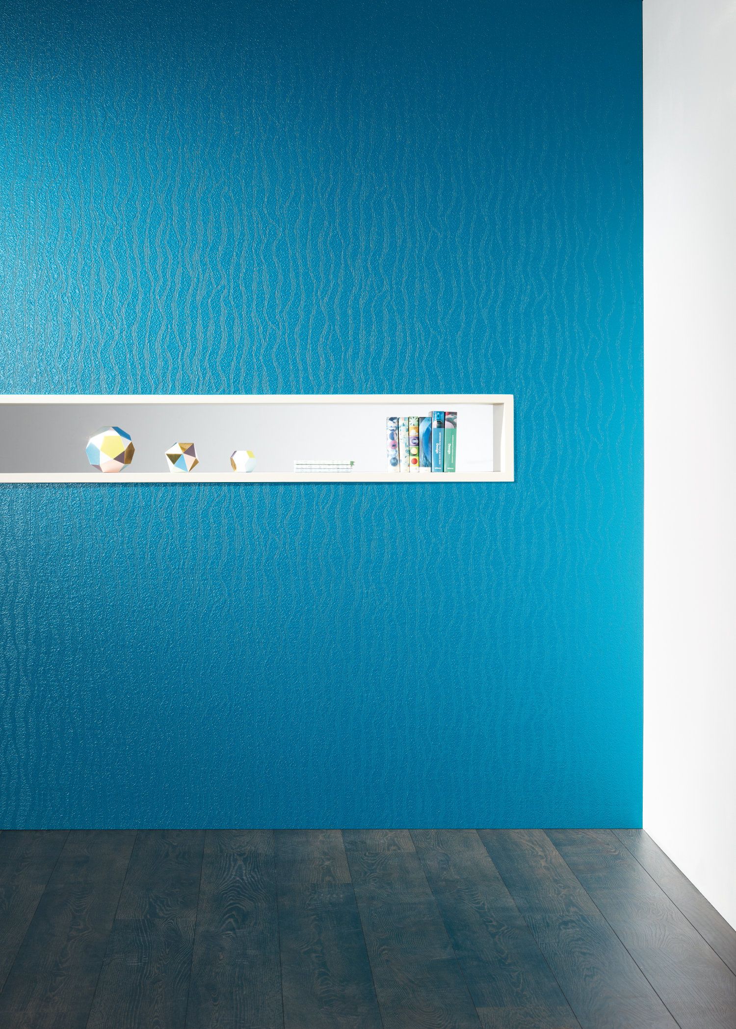 Blau strukturierte Wand mit eingebautem weißem Regal, das geometrische Dekorationsobjekte und einige Bücher enthält, dunkler Holzboden