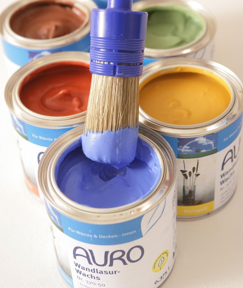 Pinsel mit blauer Farbe in Dose, umgeben von Farbdosen in Braun, Rot, Gelb und Grün